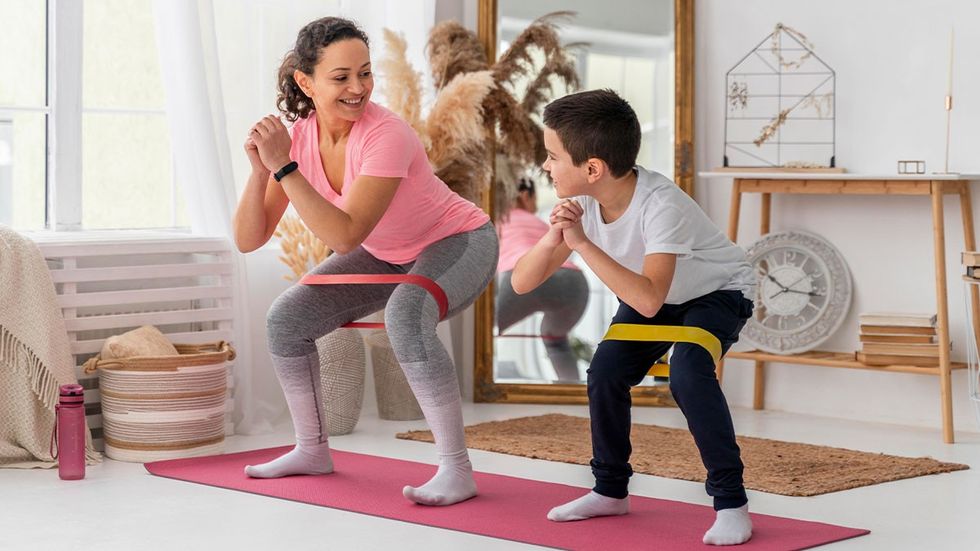 a mother and a young boy do squats in their living room