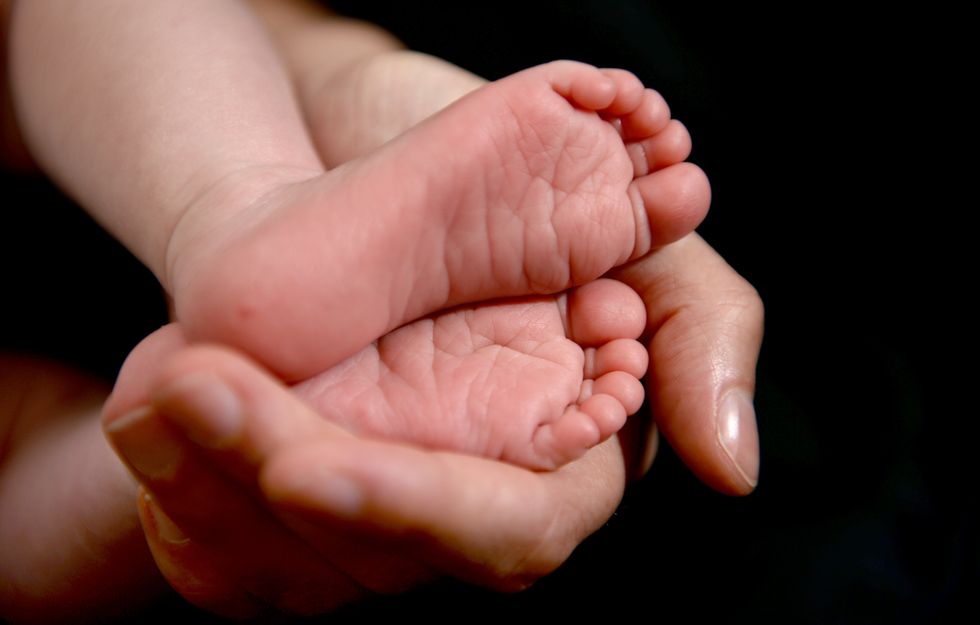 A mother cradles the feet of her new born baby in her hand