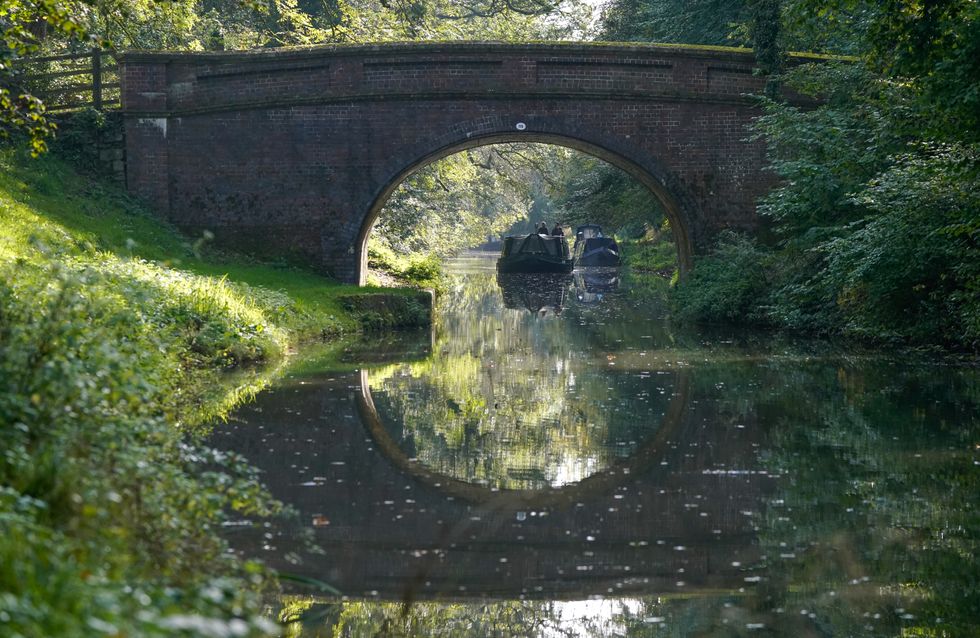 A narrow boat is driven along the Kennet & Avon Canal near to Pewsey in Wiltshire.