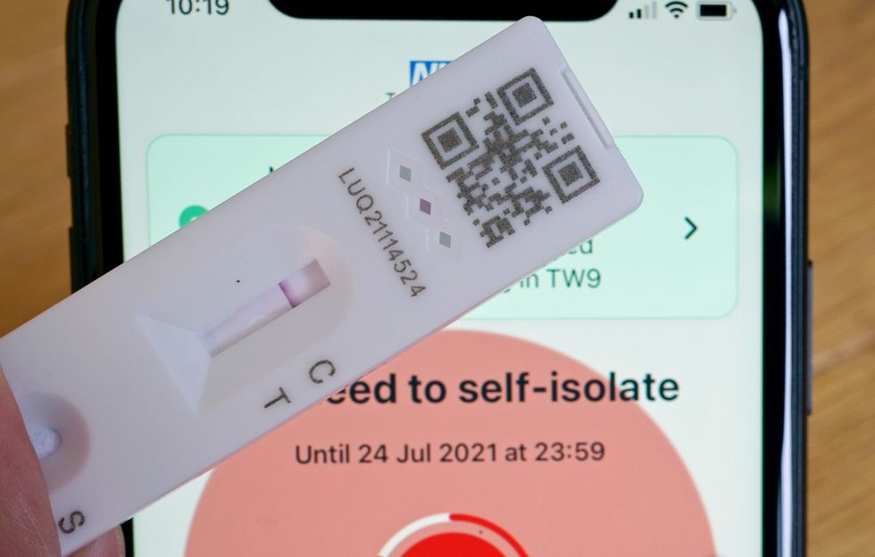 A negative lateral flow test next to advice from the NHS COVID app on an iphone to self isolate.