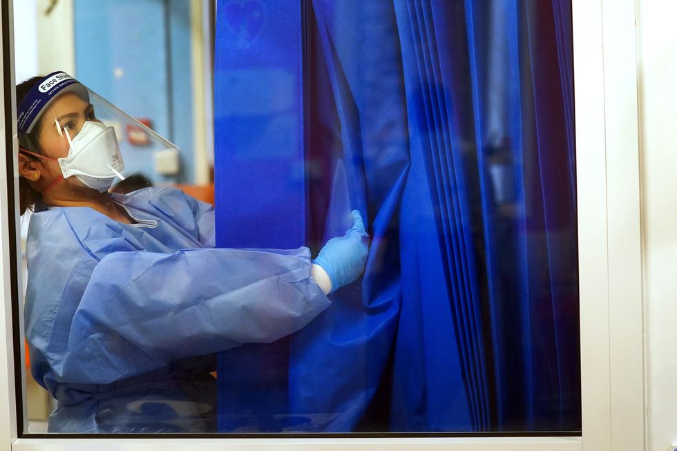 A nurse wearing full PPE adjusts a curtain on a ward for Covid patients at King's College Hospital, in south east London. Picture date: Tuesday December 21, 2021.