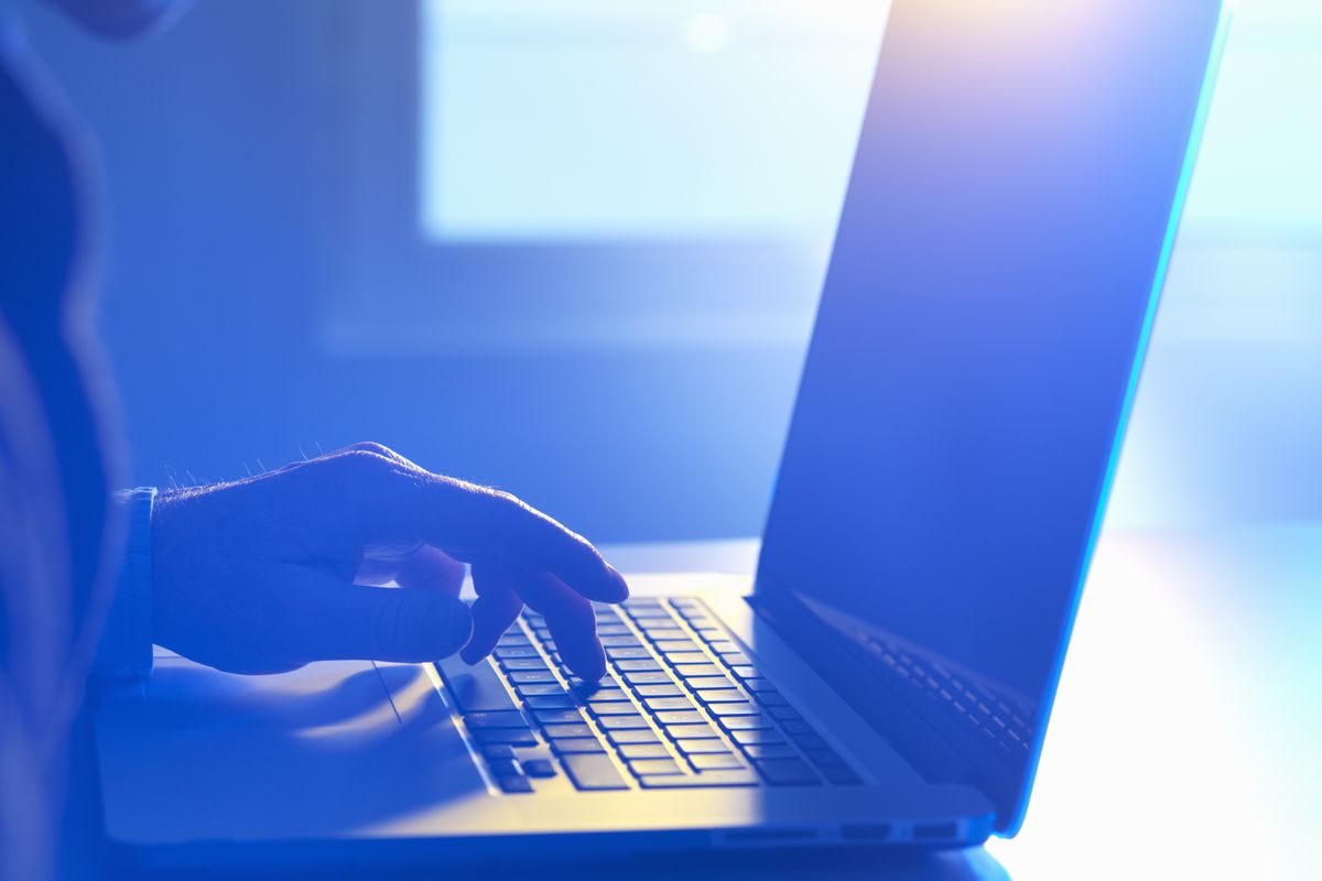 a out-of-focus man  types on a laptop with harsh blue lighting from behind 