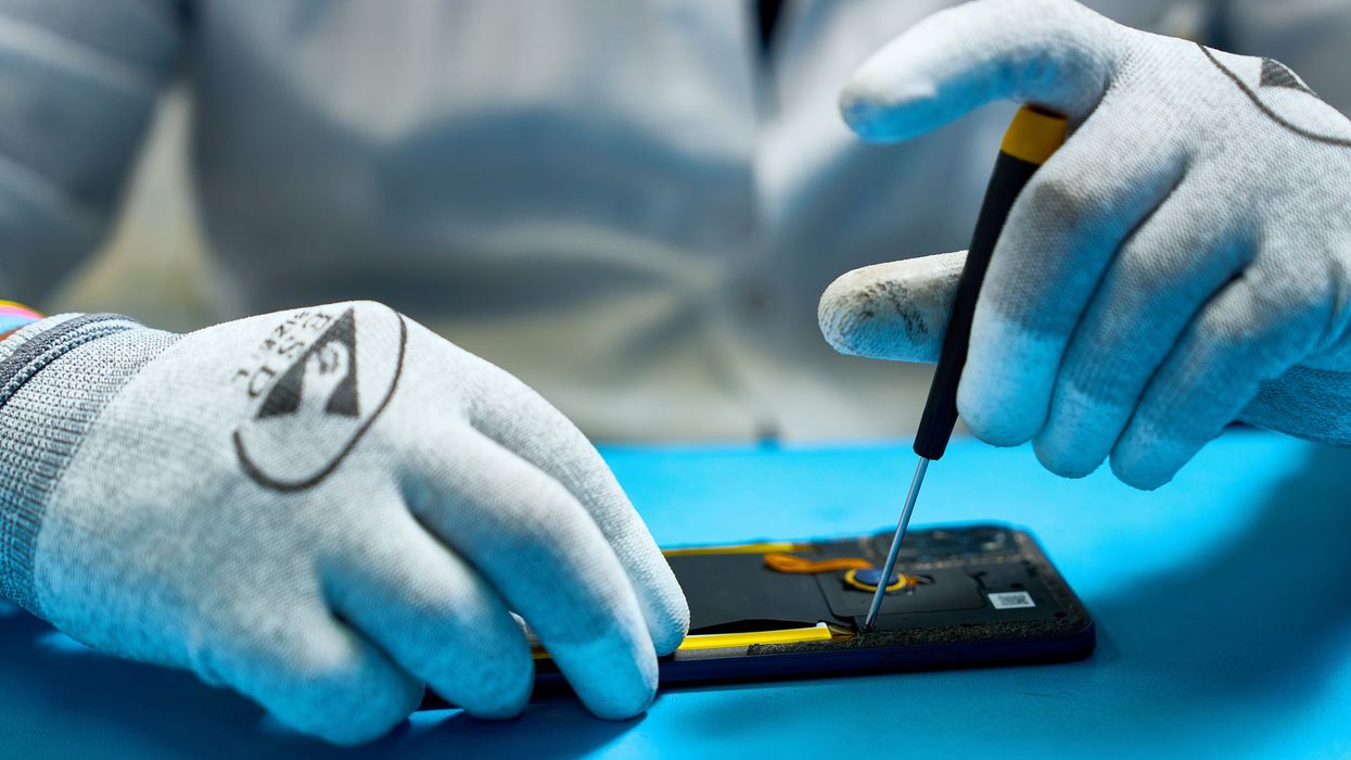 a pair of gloved hands are pictured repairing a broken smartphone on a blue table