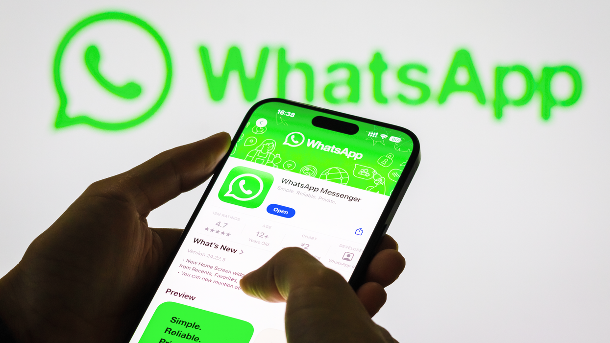 a pair of hands holds a newer iPhone model with Face ID looking at the Apple Store listing for WhatsApp