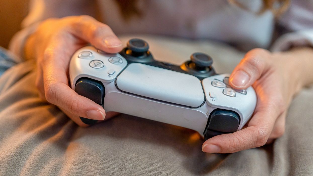 a pair of hands pictured holding a PlayStation 5 controller on a blanket