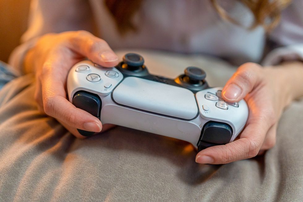 a pair of hands pictured holding a PlayStation 5 controller on a blanket 