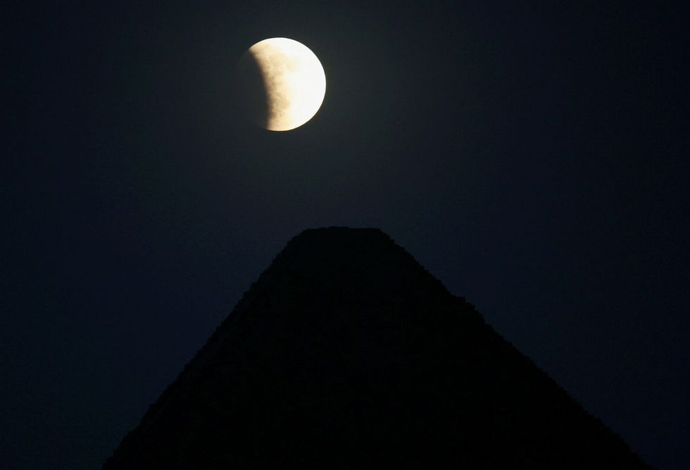 A partial eclipse appears in the sky, behind the Pyramids of Giza in Egypt