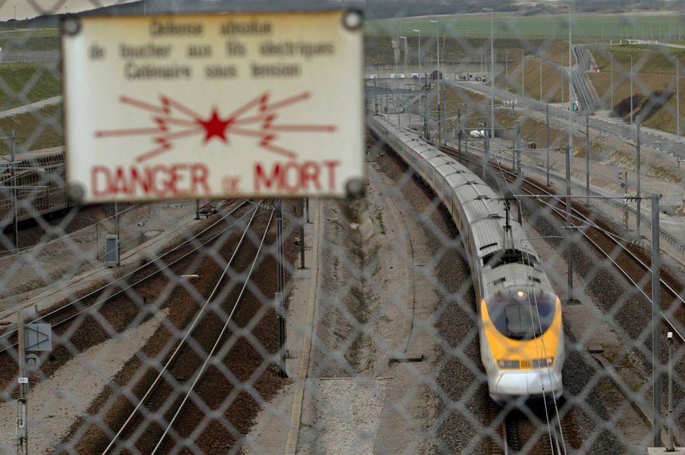 A perimeter fence sign warns of danger of death as a Eurostar passenger train exits