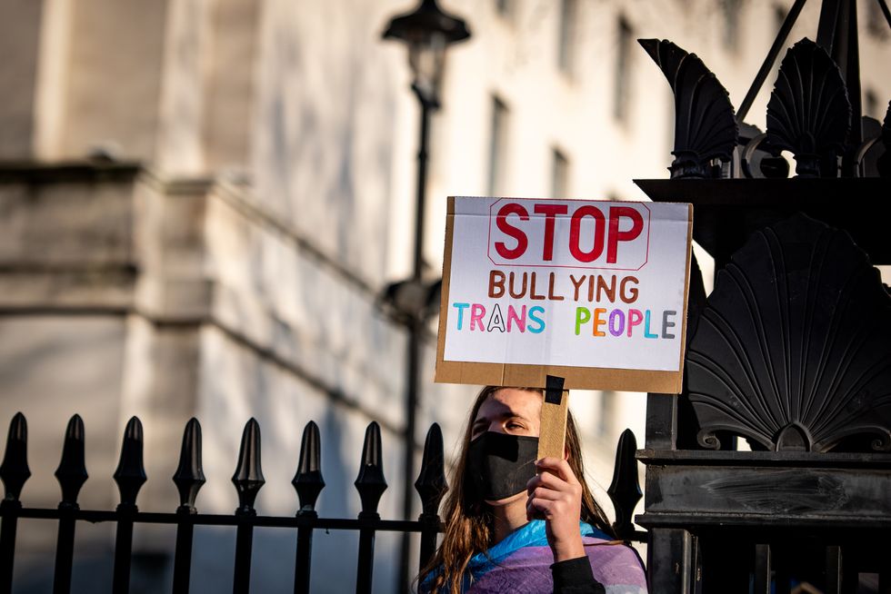 A person holding a protest sign reading "Stop bulling trans kids"