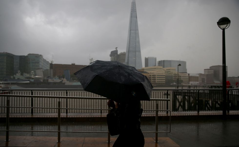 A person holding an umbrella walks next to the River Thames in London, near to The Shard, during a down pour.