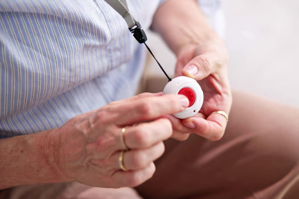 a person holding one of the red telecare personal alarms on a lanyard