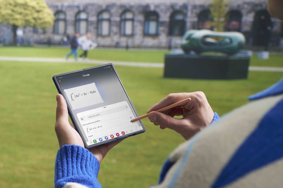 a person holds the galaxy z fold 6 in one hand and uses the s pen stylus in another to draw and write on the screen