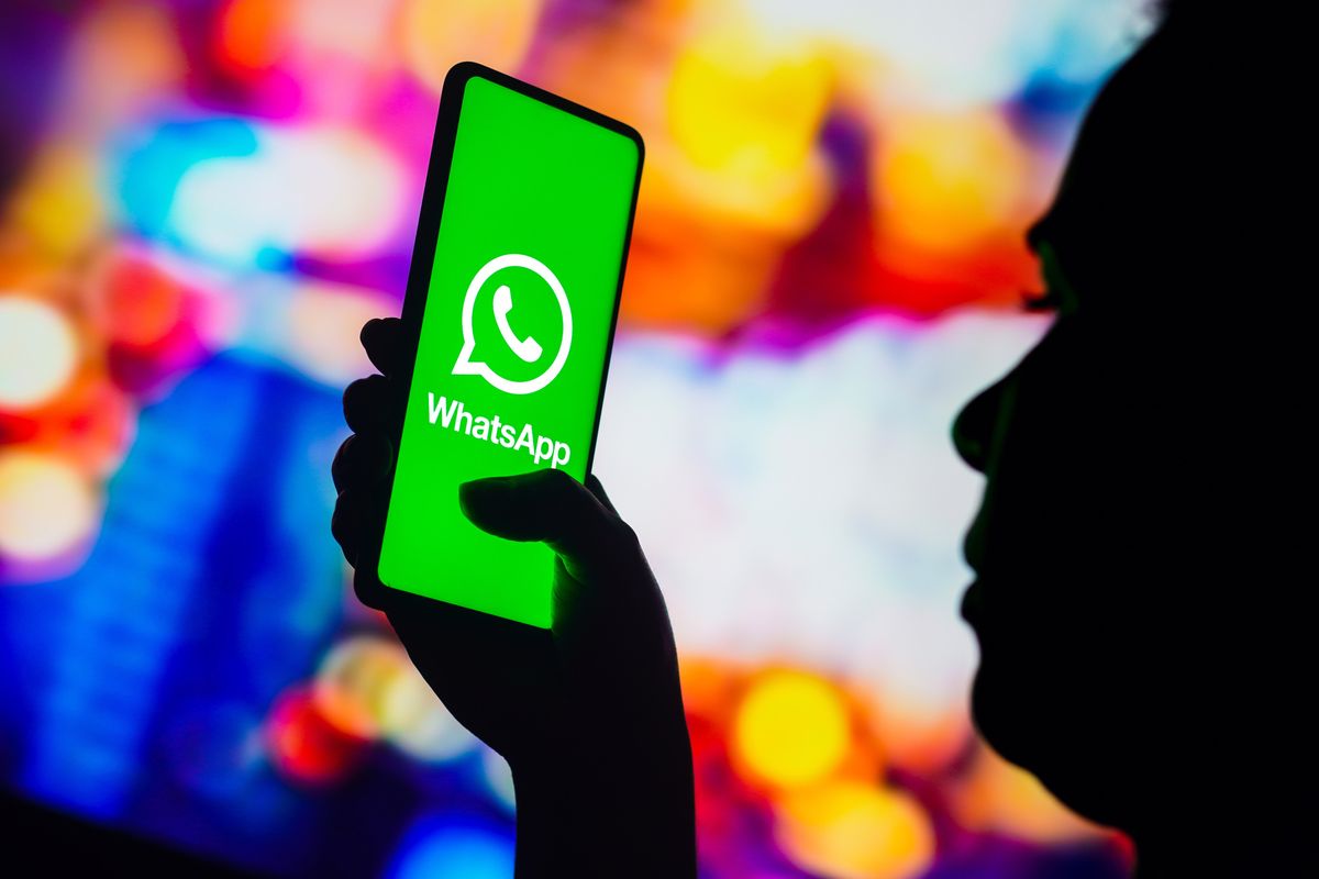 a person in silhouette holds a smartphone with the whatsapp logo on screen 