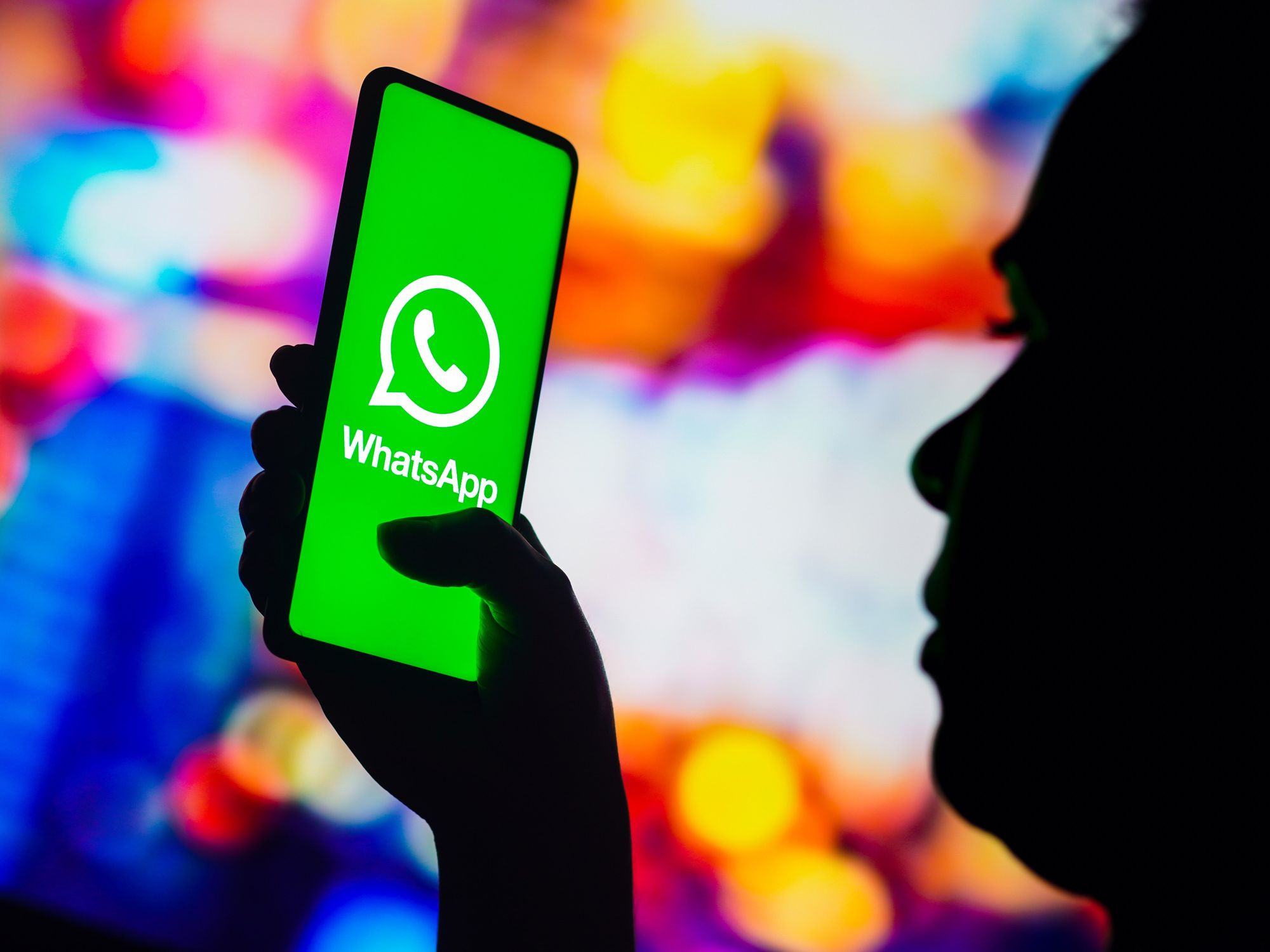 a person in silhouette holds a smartphone with the whatsapp logo on screen