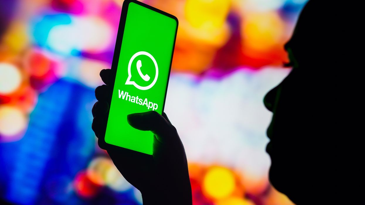 a person in silhouette holds a smartphone with the whatsapp logo on screen