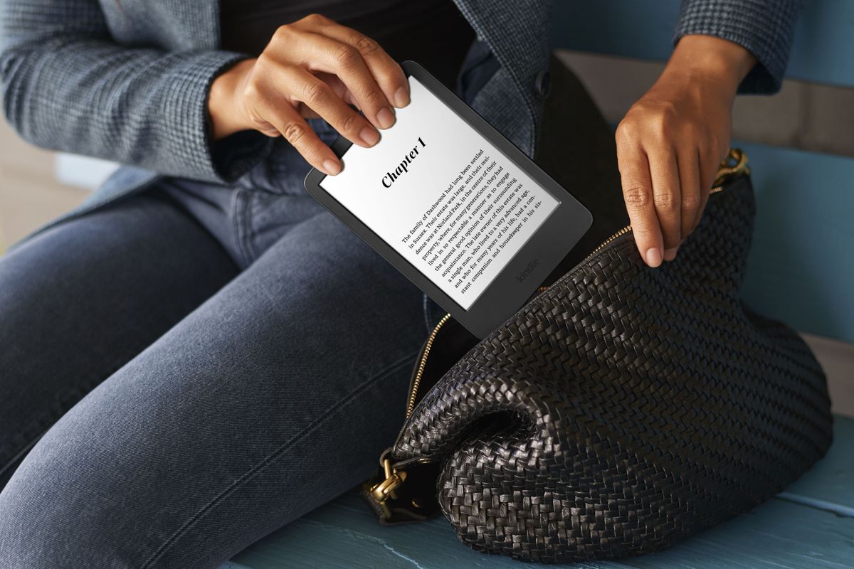 a person is pictured putting an amazon kindle paperwhite with the screen illuminated into a bag  