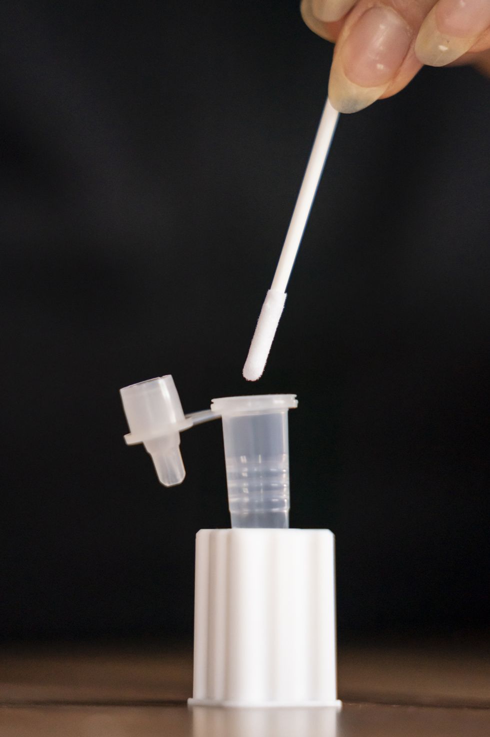 A person placing a swab from a Covid 19 lateral flow test into a buffer tube contusing testing solution