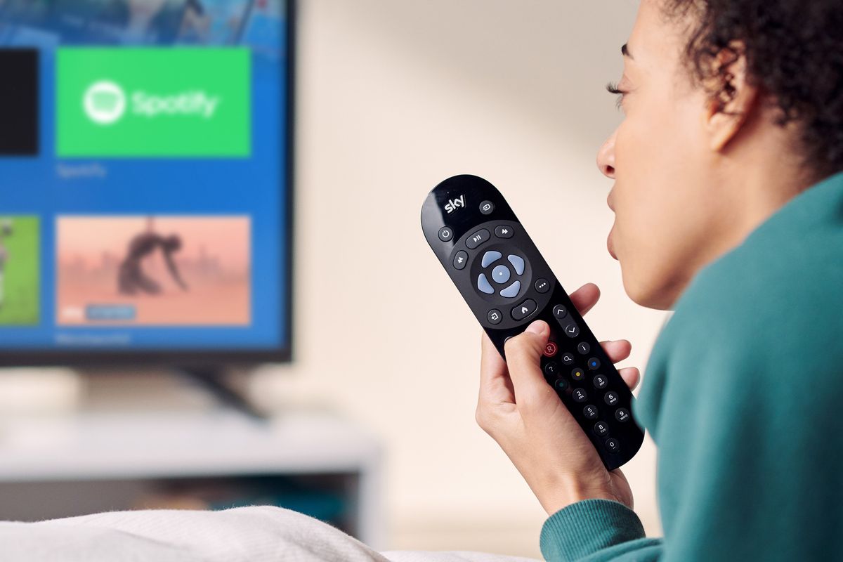 a person reclines on a sofa with the sky tv remote in their hand