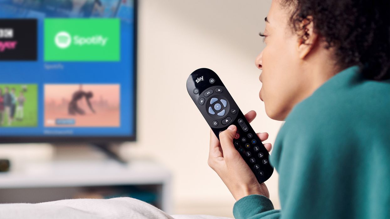 a person reclines on a sofa with the sky tv remote in their hand
