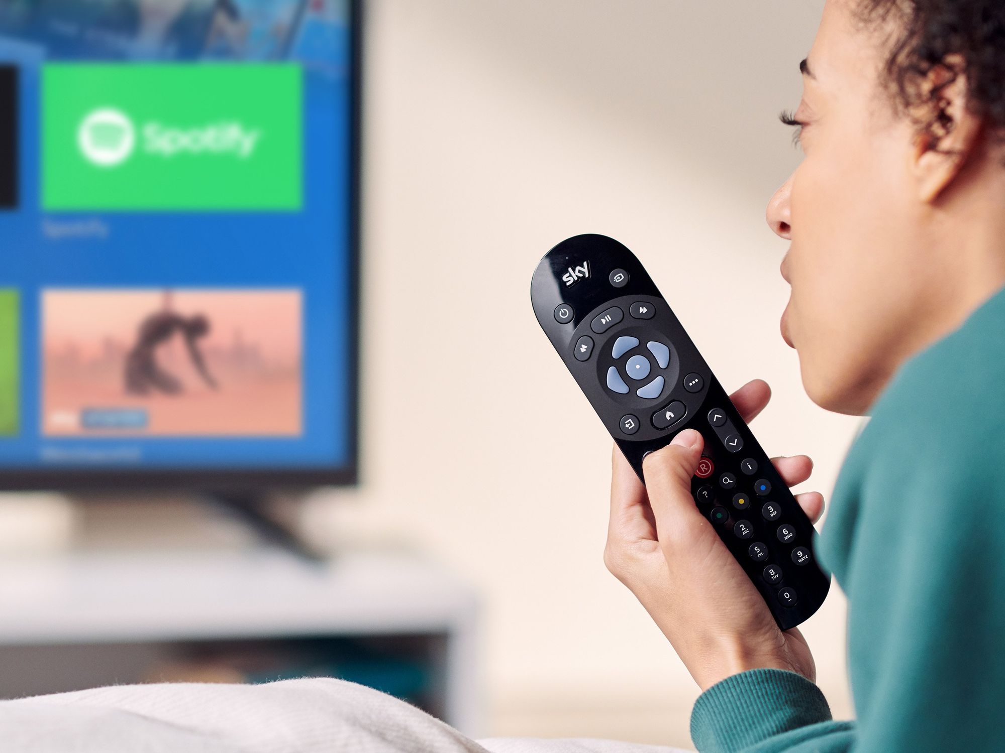 a person reclines on a sofa with the sky tv remote in their hand