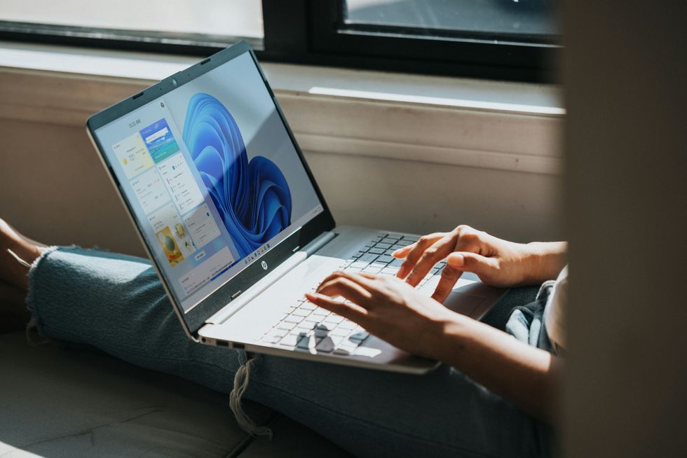 a person sits with a laptop on their knees using the trackpad to navigate around windows 11 on-screen 