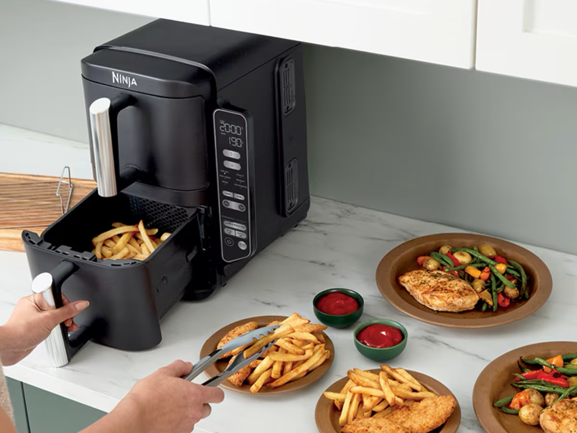 a person uses tongs to remove fries from the Ninja Double Stack Air Fryer on a kitchen countertop