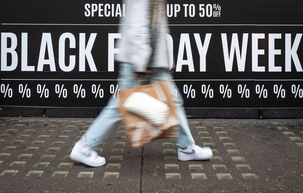 a person with shopping bags walks past a sign advertising black friday sales and discounts