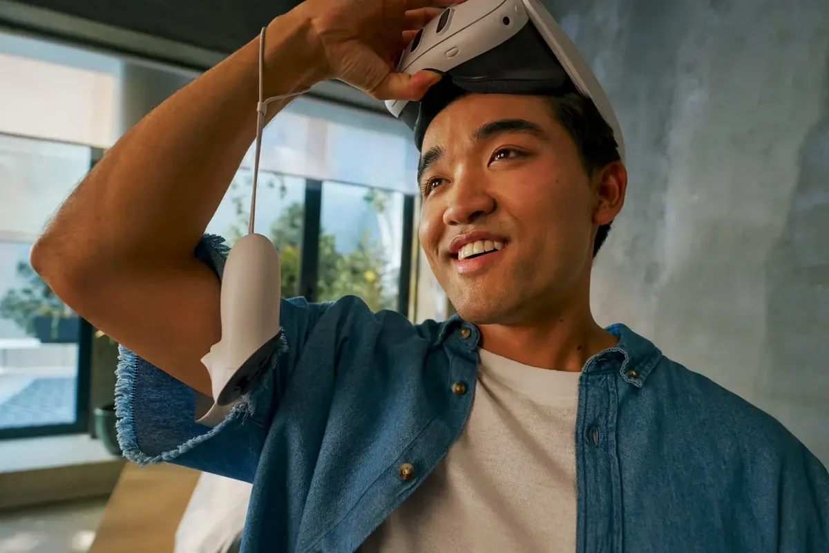 a picture of a man lifting up the meta quest 3 headset from his eyes with a controller dangling on his arm 
