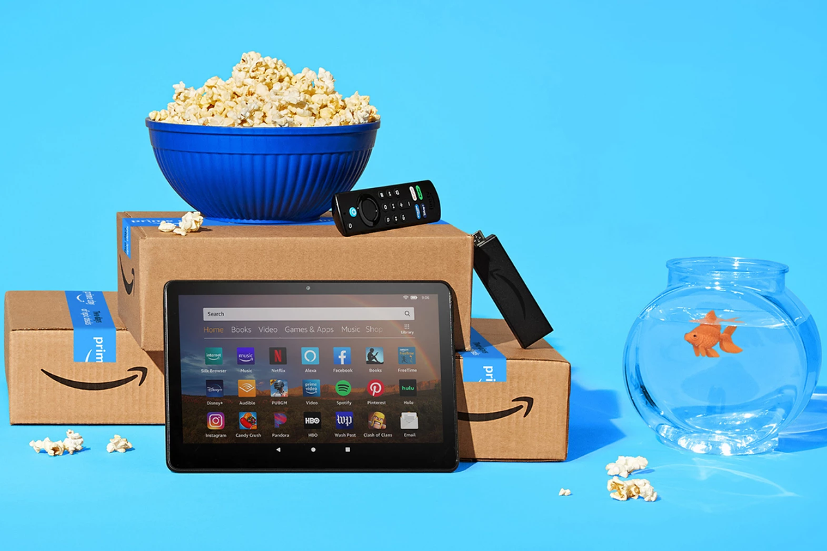 a pile of amazon prime boxes with a fire tablet, fire tv stick remote and popcorn littered on the blue background 