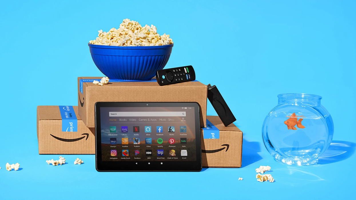 a pile of amazon prime boxes with a fire tablet, fire tv stick remote and popcorn littered on the blue background