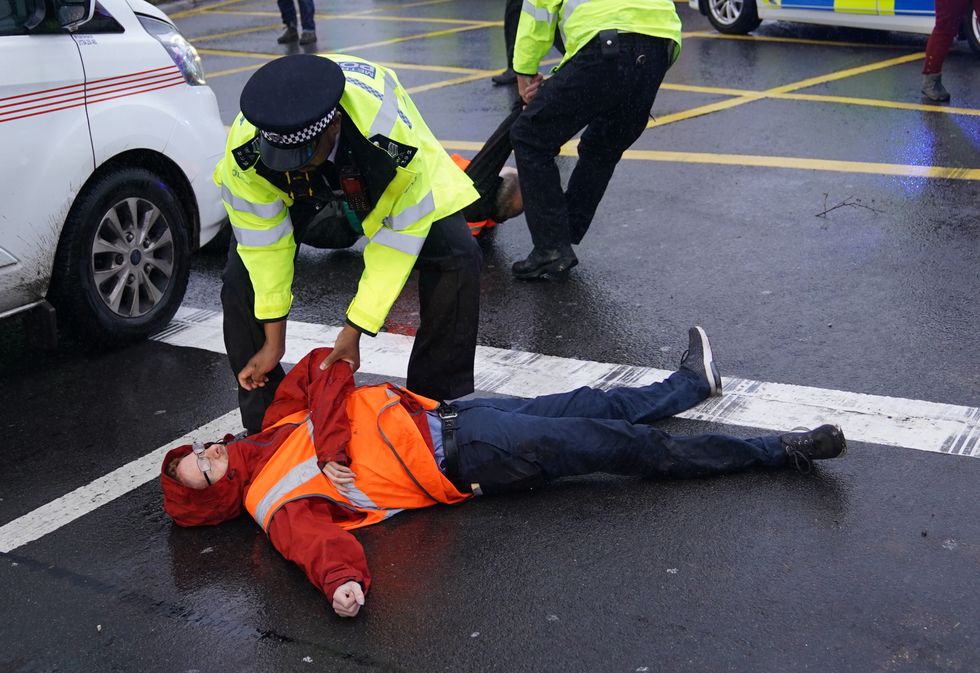 A police officer detains a protester from Insulate Britain occupying a roundabout leading from the M25 motorway to Heathrow Airport in London. Picture date: Monday September 27, 2021.
