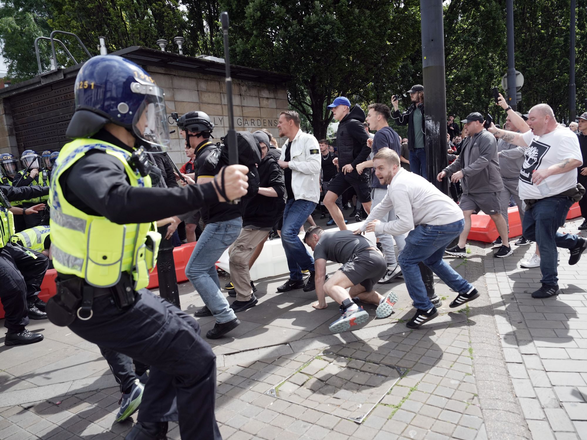 a police officer holds a baton as men scramble on the pavement
