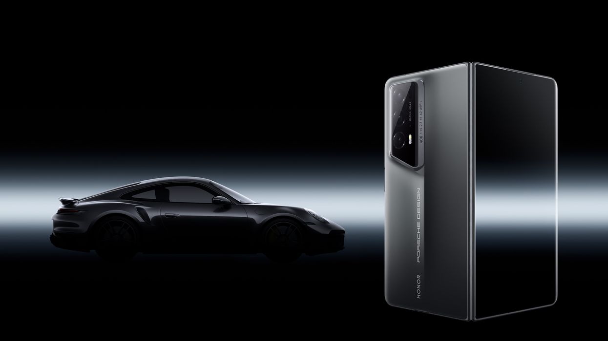 a porsche 911 is pictured in the background behind an honor magic v2 folding phone
