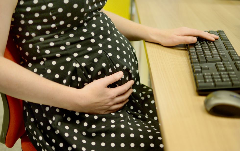A pregnant office worker cradles her bump, London