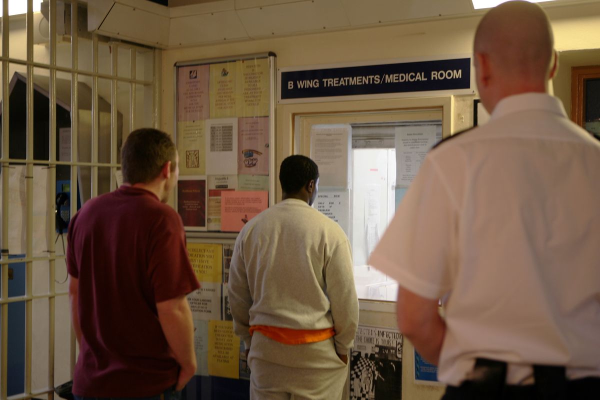 A prison officer watches prisoners as they collect their medication