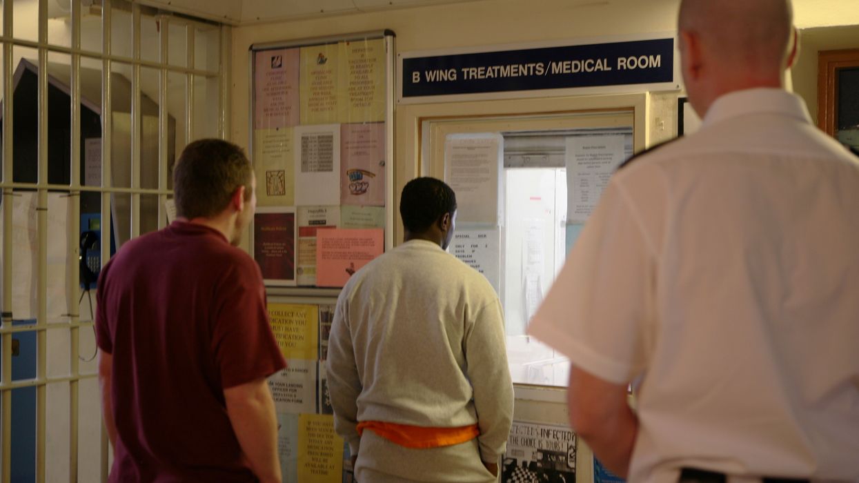 A prison officer watches prisoners as they collect their medication