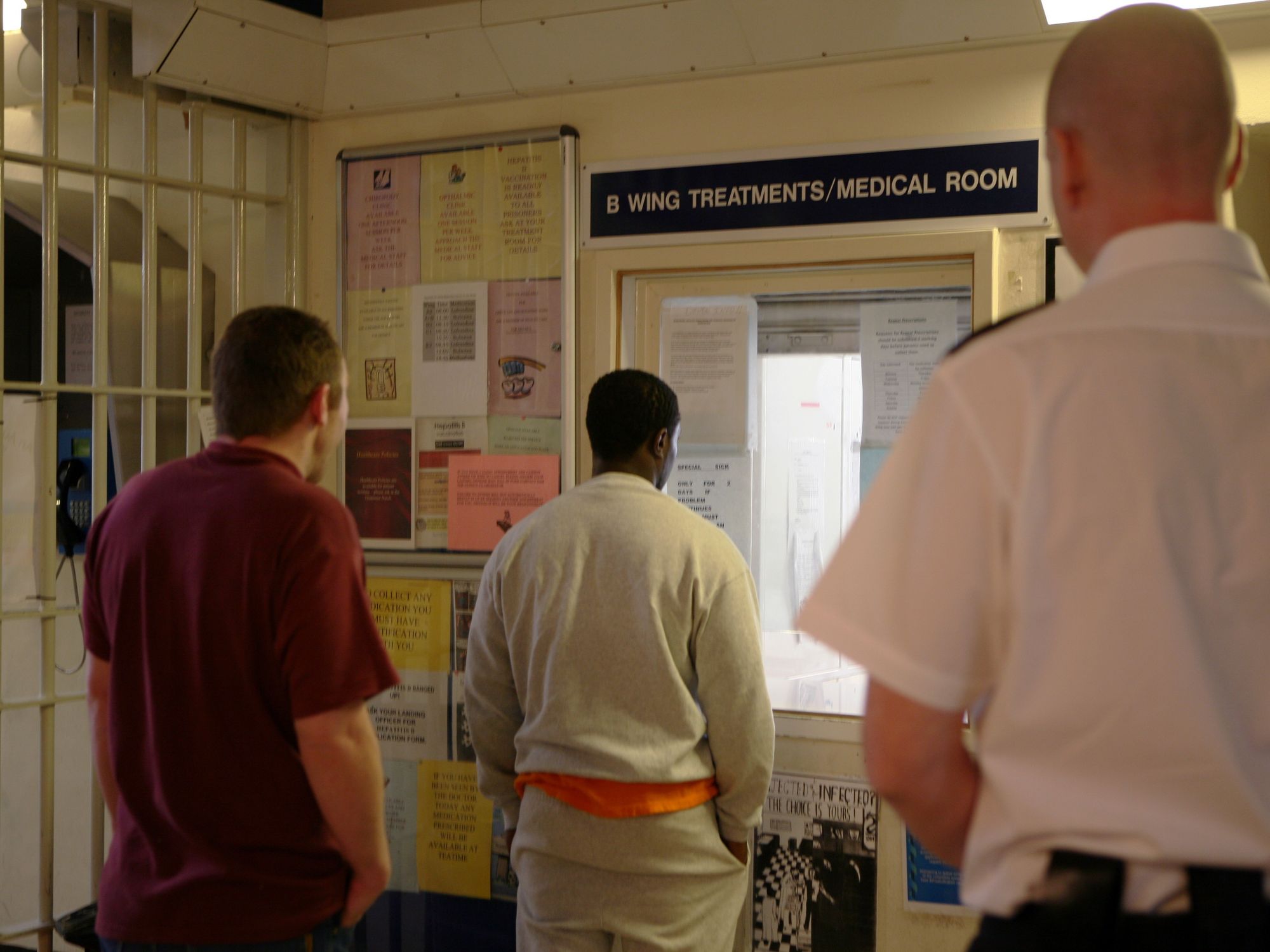 A prison officer watches prisoners as they collect their medication