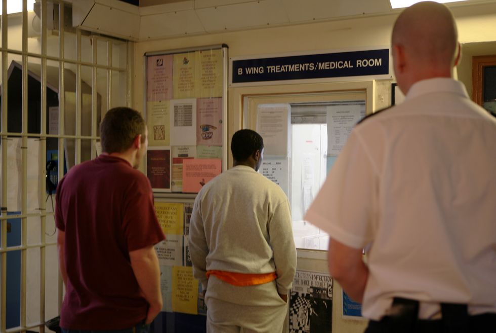 A prison officer watches prisoners as they collect their medication