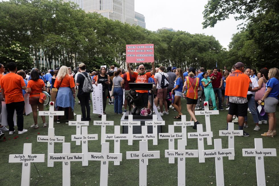 A protester holds a sign behind the crosses with names of victims of Uvalde, Texas shooting, during \%22March for Our Lives\%22 rally, one of a series of nationwide protests against gun violence, at Cadman Park Plaza in Brooklyn, in New York City, US.