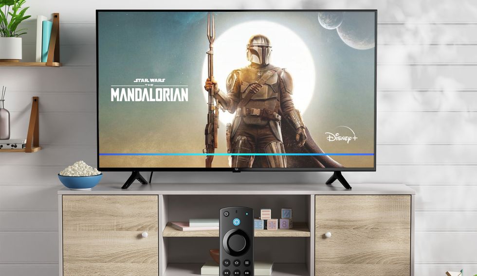 a remote control for the fire tv is shown using voice controls with alexa to select the mandalorian on disney plus