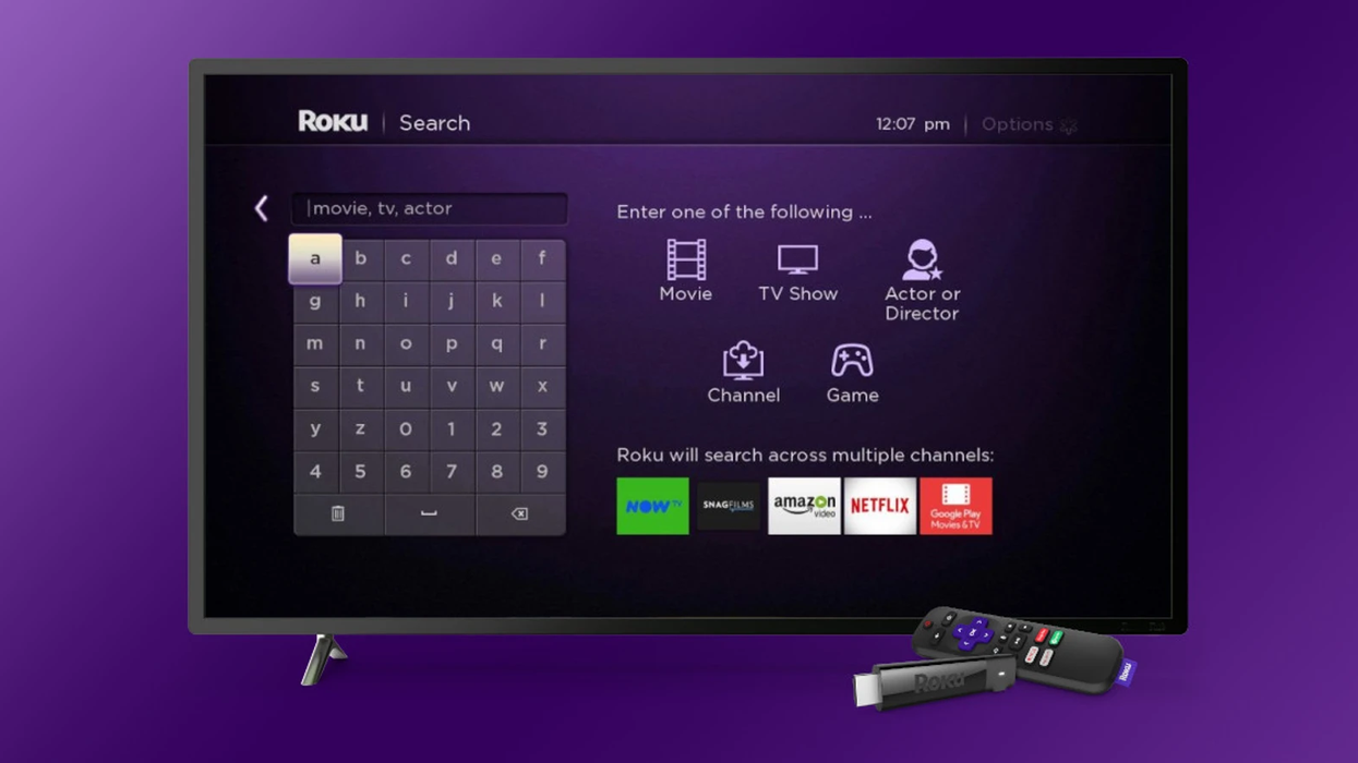a roku stream stick and remote are pictured lying in front of a smart tv running the roku search menu