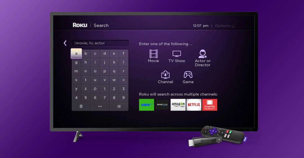 a roku stream stick and remote are pictured lying in front of a smart tv running the roku search menu 