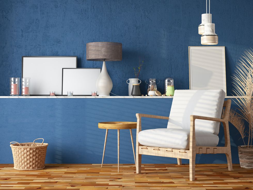 A room painted in navy blue with a lamp, table, basket and chair