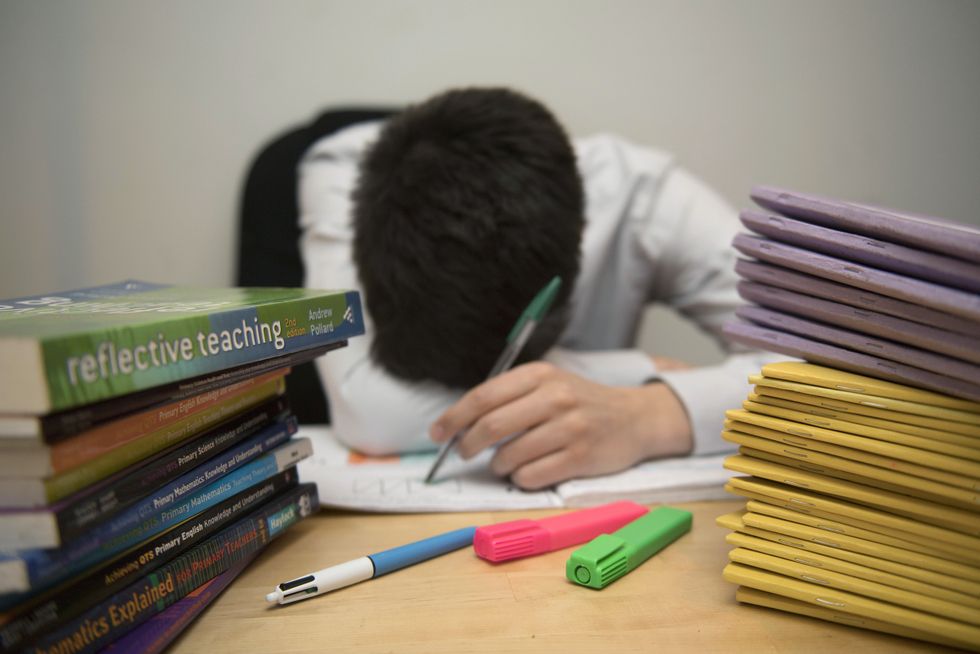 A school teacher looking stressed next to piles of classroom books, as a teacher was awarded nearly 1 million in compensation following a serious assault by a pupil, a union has revealed