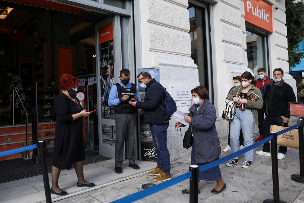 A shop employee checks customers’ vaccination certificates against Covid-19, as the government imposed further measures for unvaccinated citizens, in Athens, Greece