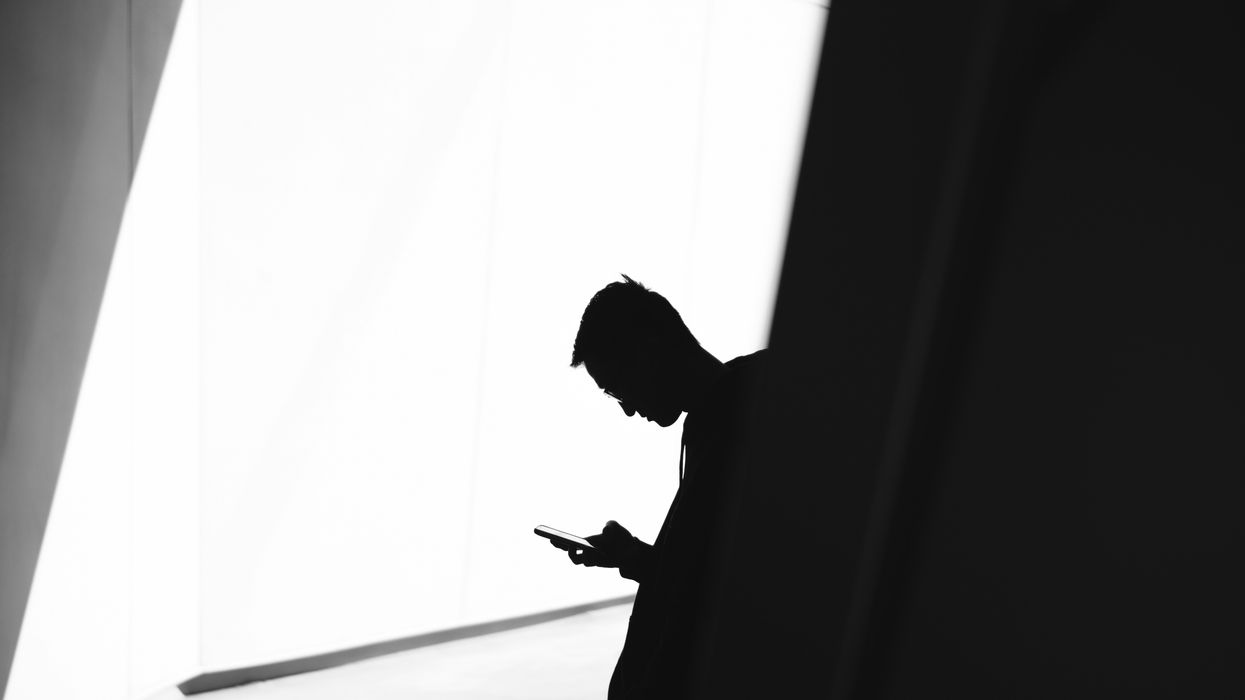 a silhouetted man is pictured checking a smartphone in the shadows