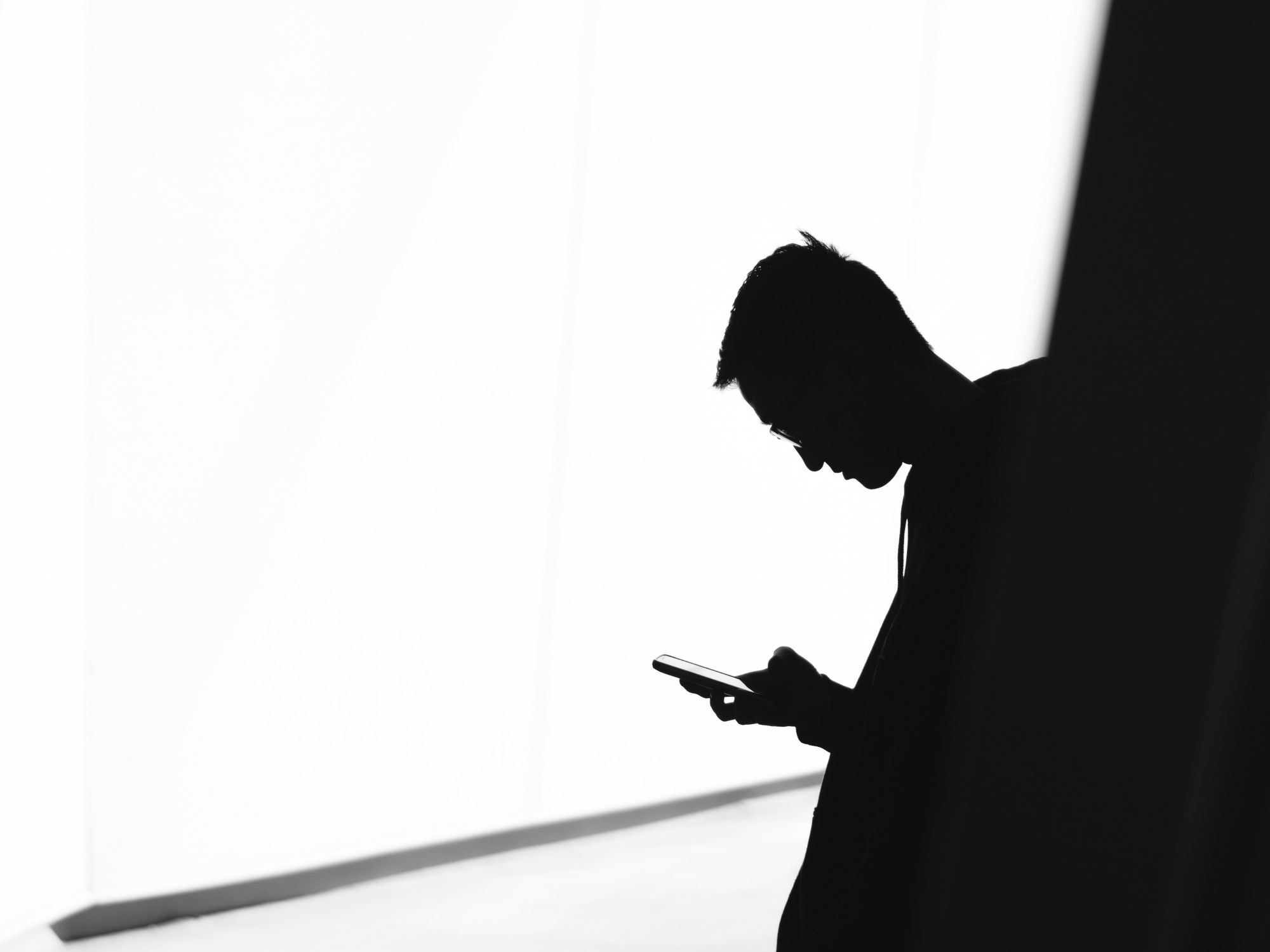 a silhouetted man is pictured checking a smartphone in the shadows