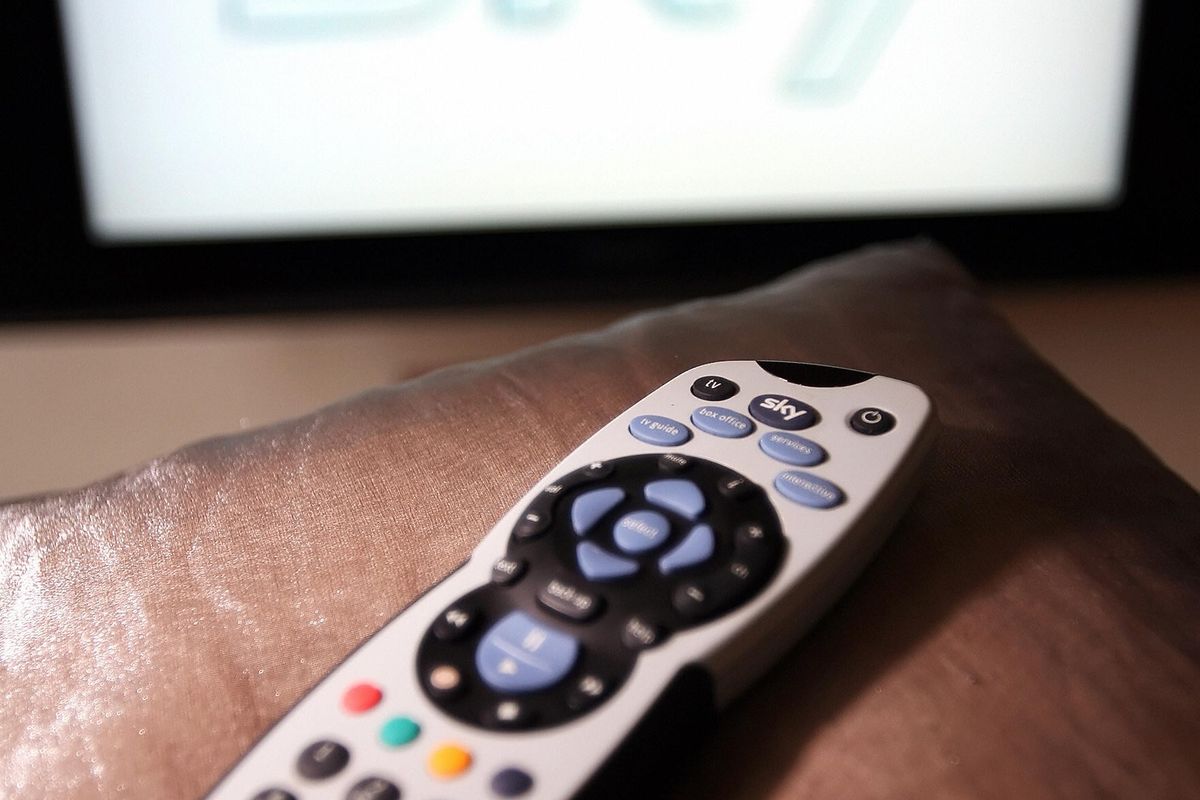 a sky plus remote lying on the arm of a sofa with the sky logo on a television screen in the background  