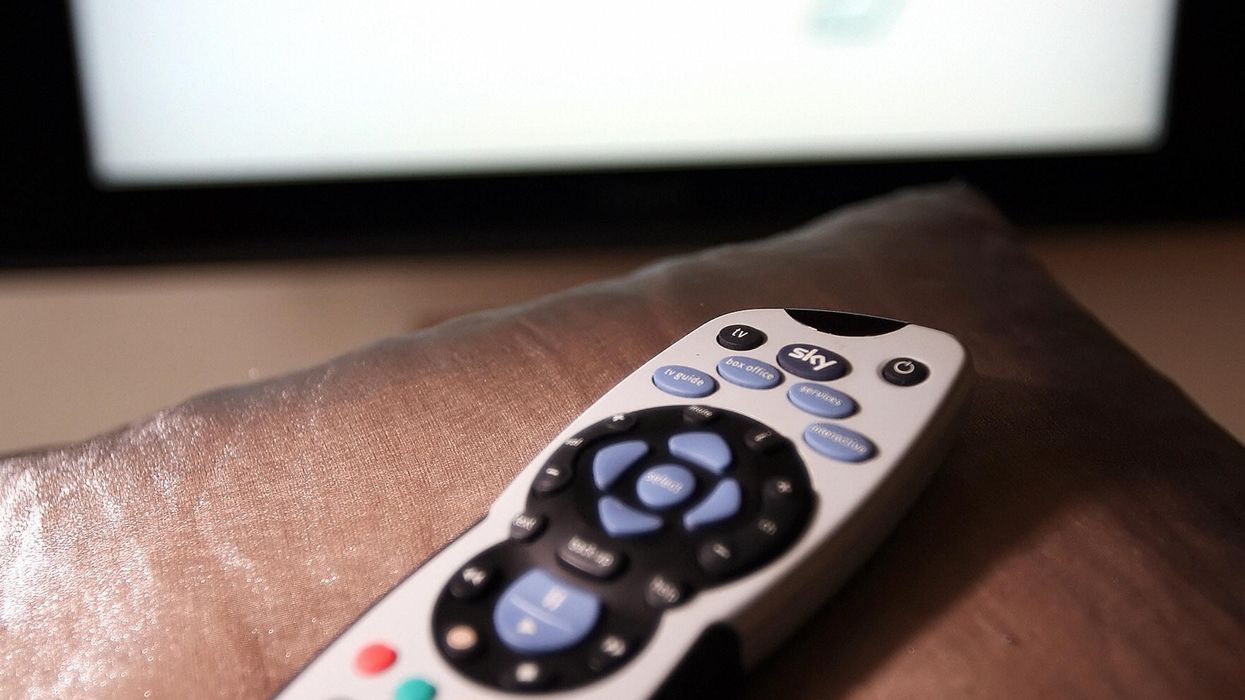 a sky plus remote lying on the arm of a sofa with the sky logo on a television screen in the background