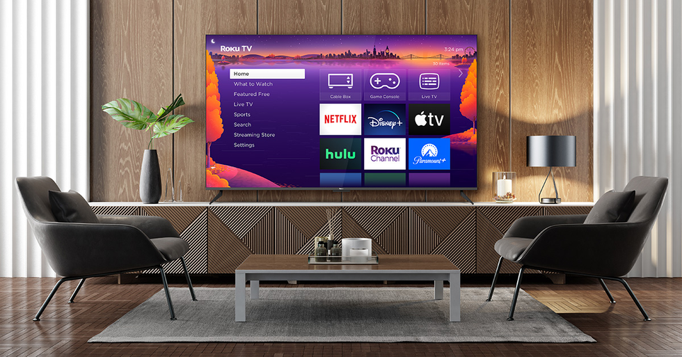 a smart tv running roku software is pictured on the wall of an office with two chairs and a table in the foreground